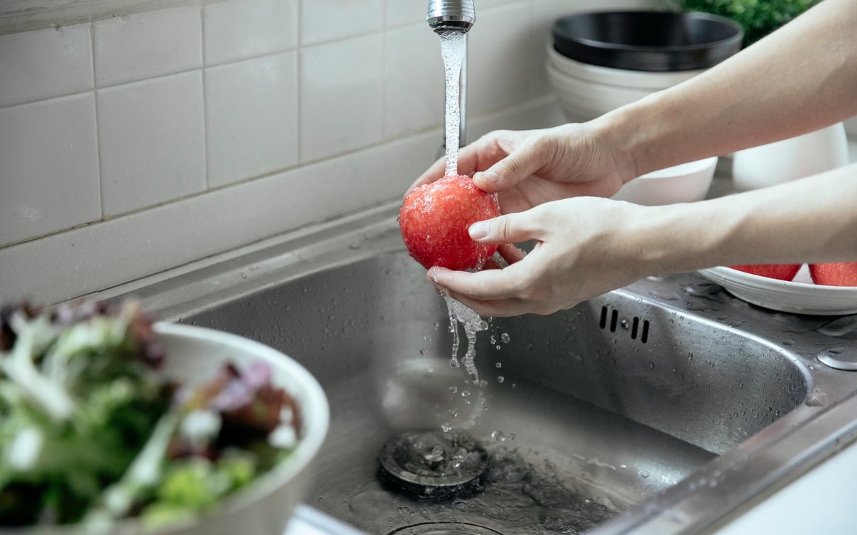 A fresh red apple being washed under running water in a kitchen sink