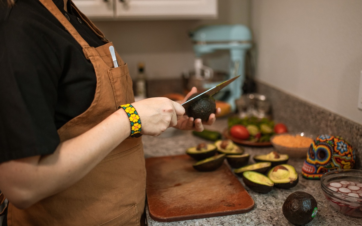 A cook slicing a ripe avocado on a kitchen cutting board