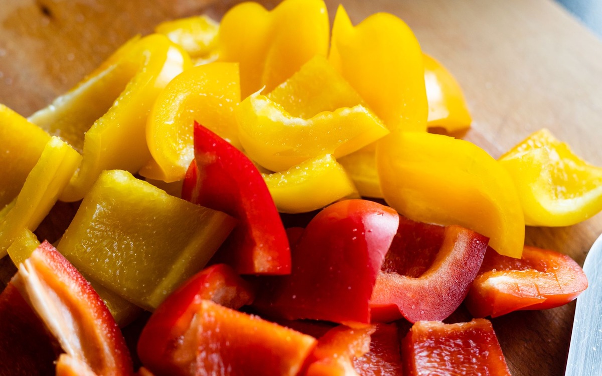 Fresh red and yellow bell pepper strips and pieces on a wooden cutting board