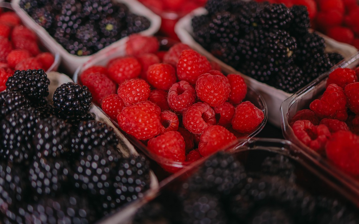 Fresh raspberries and blackberries displayed in small containers at a market