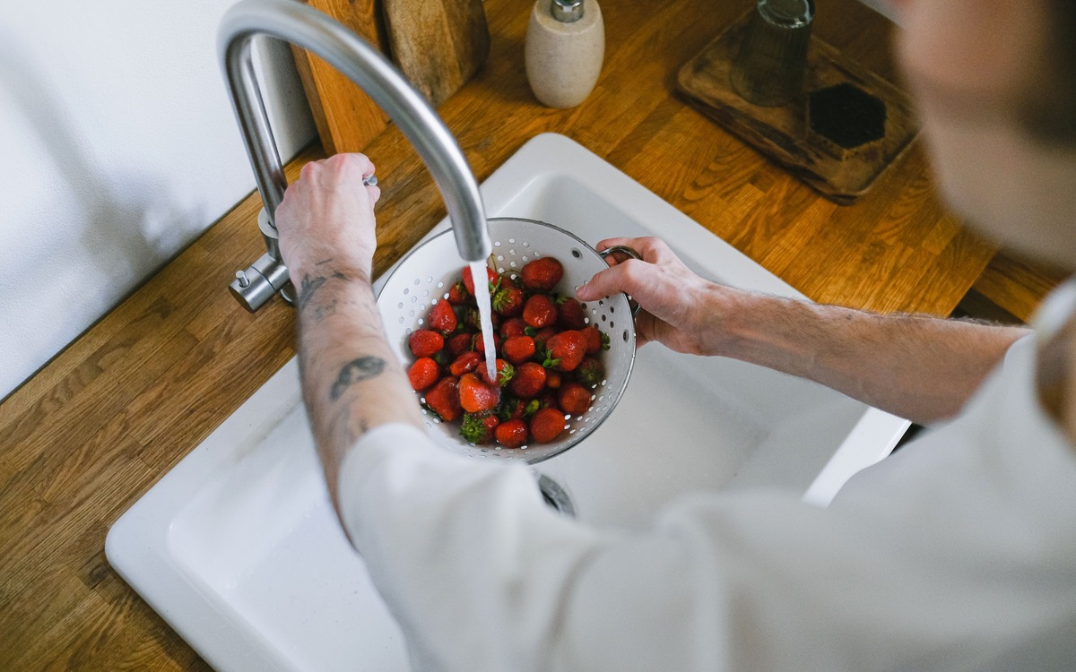 Fresh strawberries being rinsed under running water in a kitchen strainer