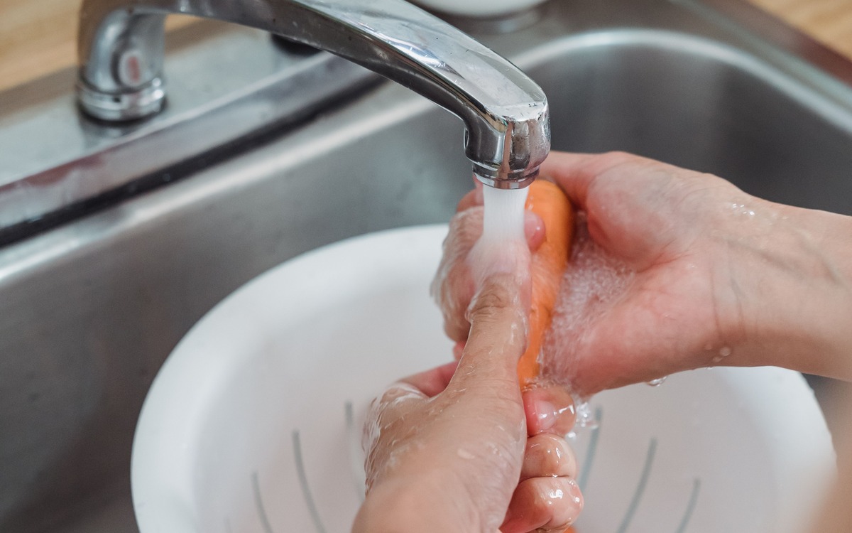 Fresh carrots being rinsed under running water in a kitchen colander