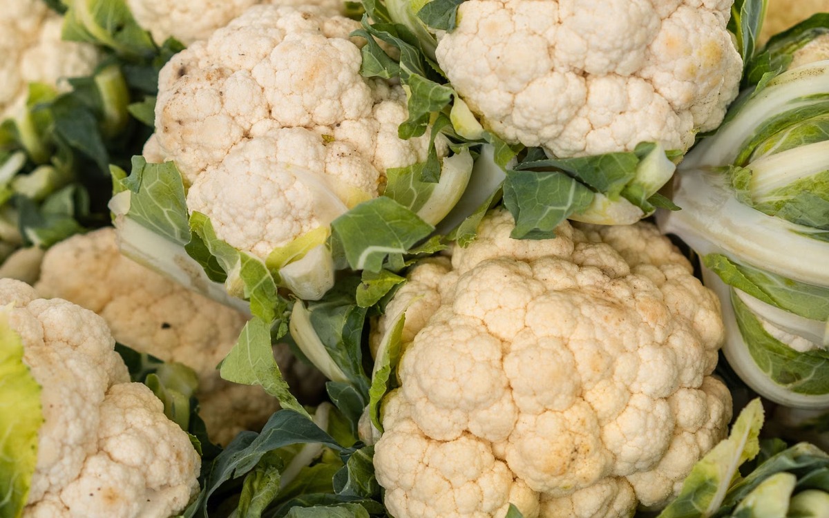 Close-up of a compact fresh white cauliflower head with green leaves