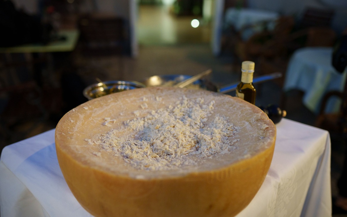 A large wheel of hard cheese being prepared for serving