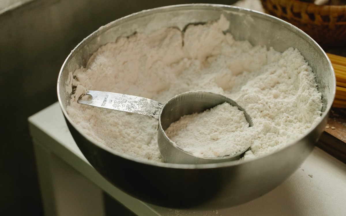 White flour in a metal bowl with a measuring cup ready for baking