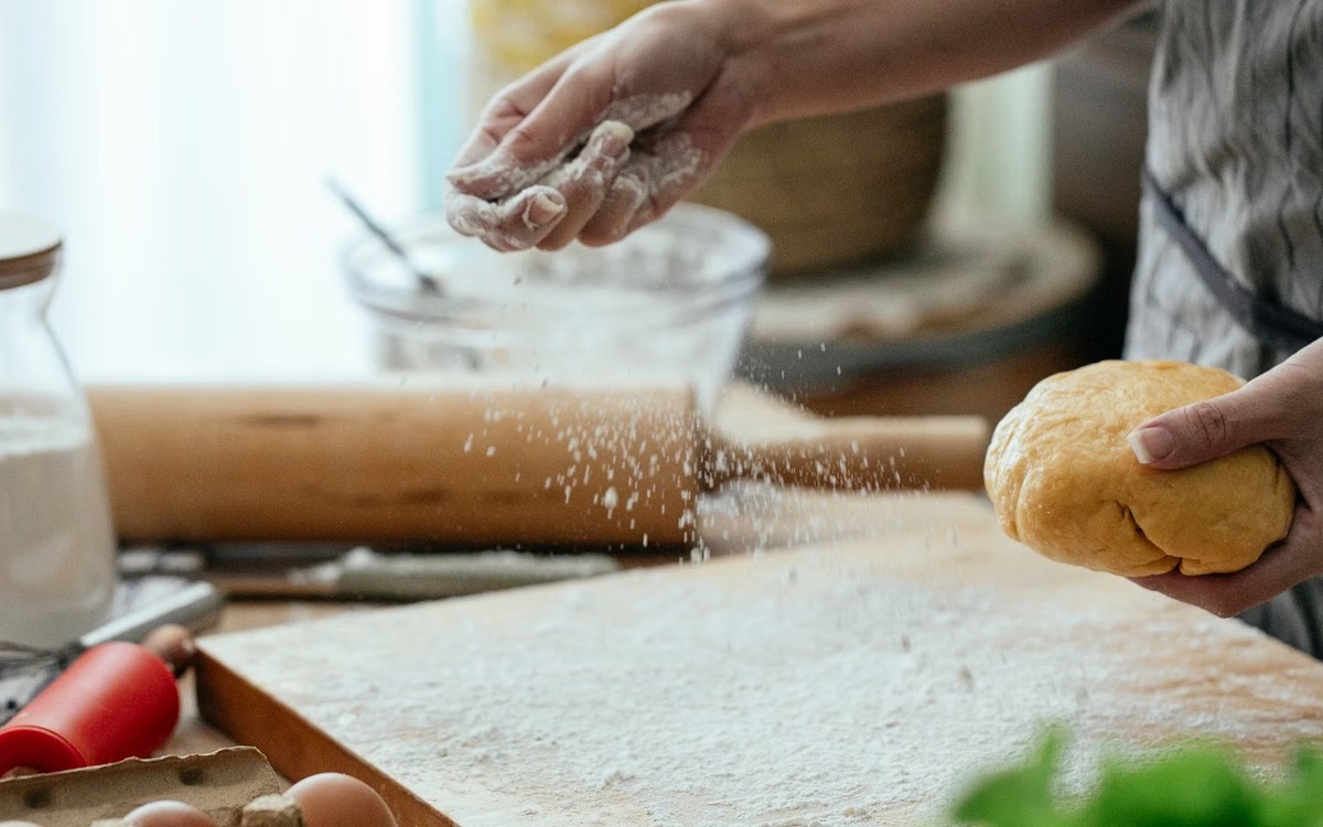 Hands working with uncooked dough and loose flour on a kitchen work surface
