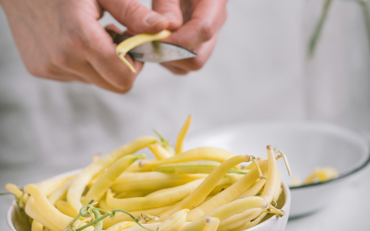 Hands preparing vegetables in a bowl on a kitchen work surface