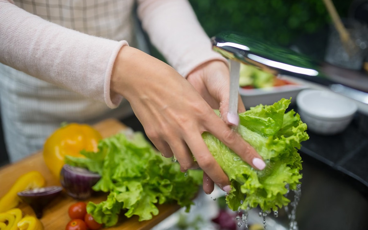 Fresh lettuce being rinsed under running water in a home kitchen