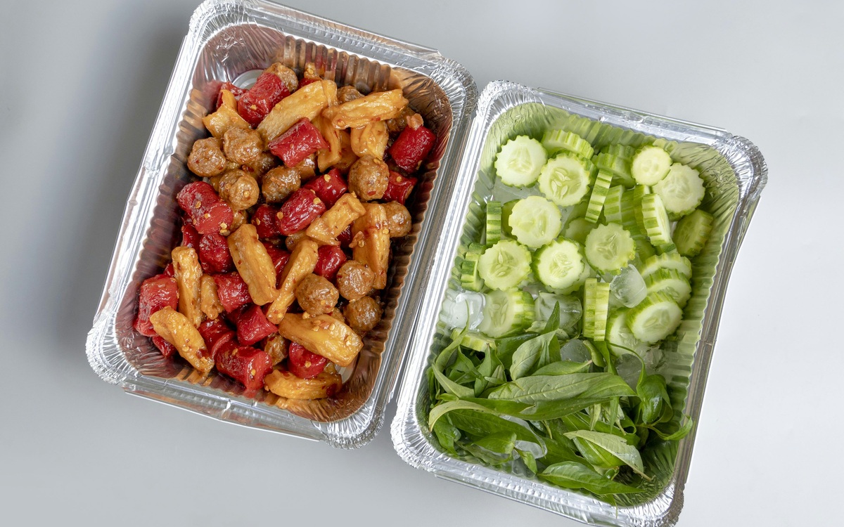 Two prepared meal containers with cooked food, cucumbers, and fresh herbs