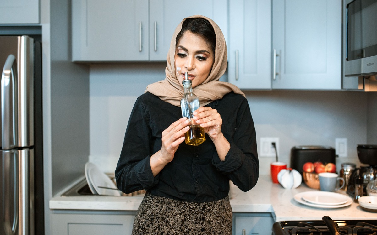 Home cook smelling olive oil from a small glass bottle in a kitchen