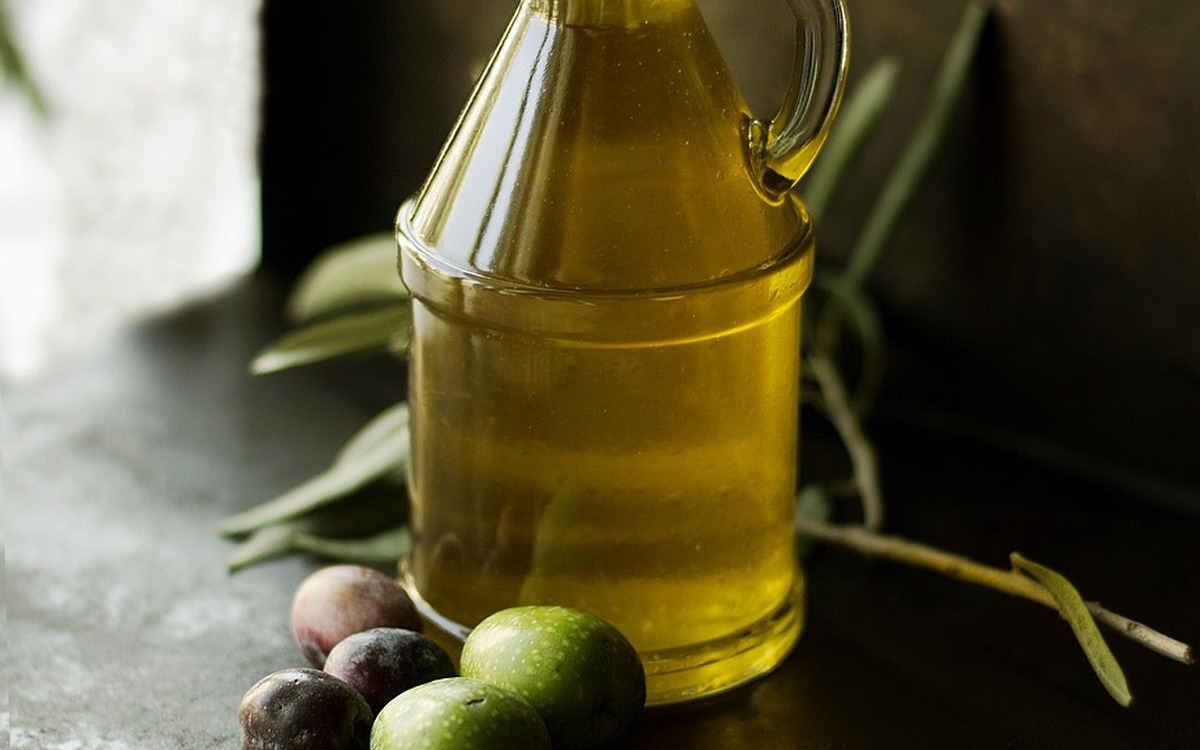 Bottle of olive oil with olives arranged on a dark surface