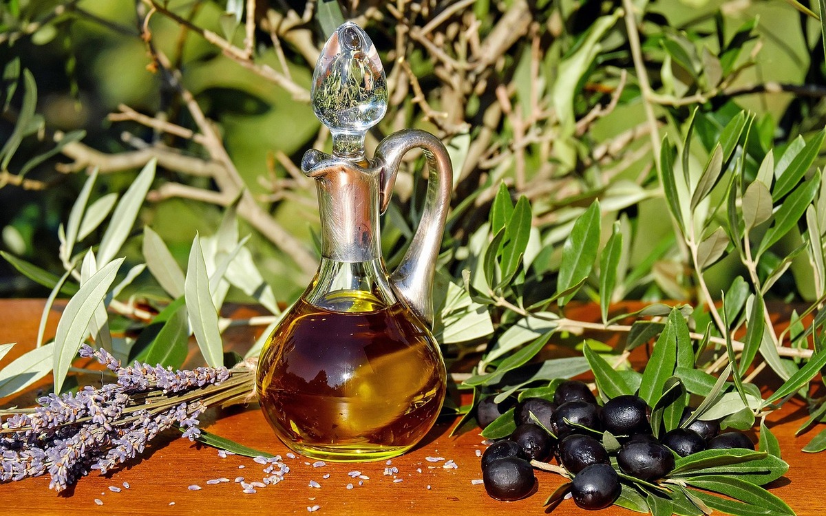 Olive oil in a glass carafe beside olives and olive branches