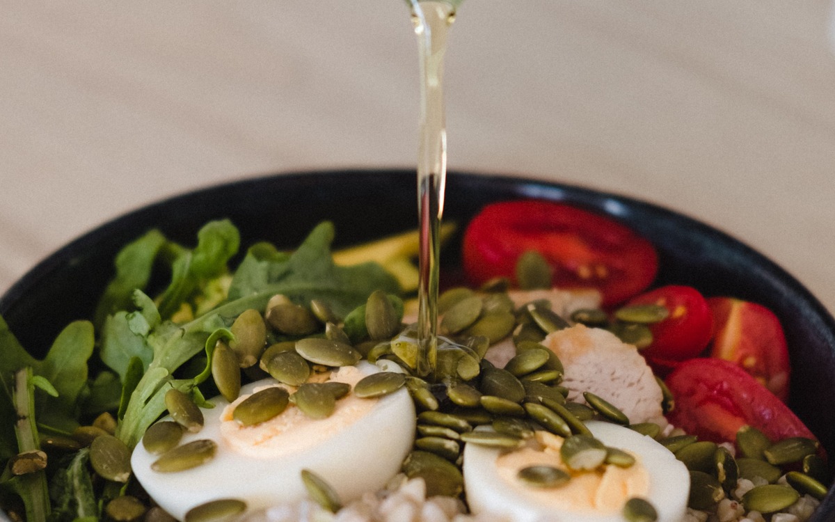 Olive oil being poured from a dark bottle over a grain and vegetable bowl