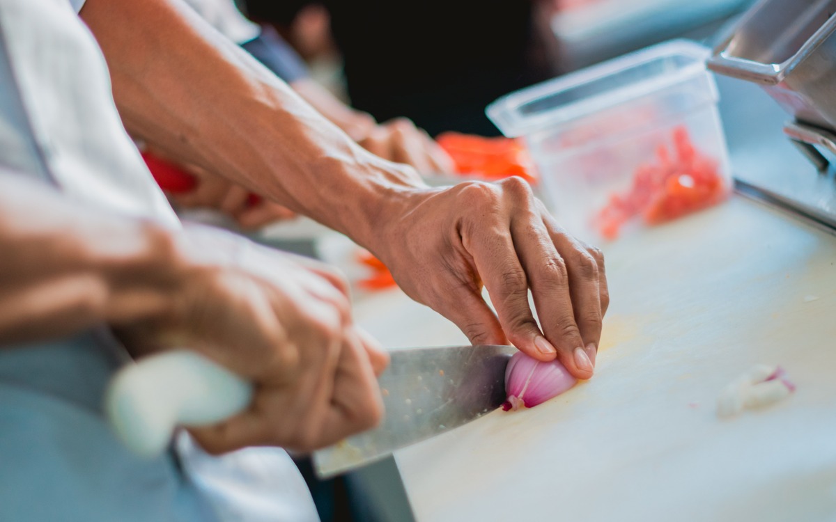 A cook slicing a fresh red onion with a kitchen knife