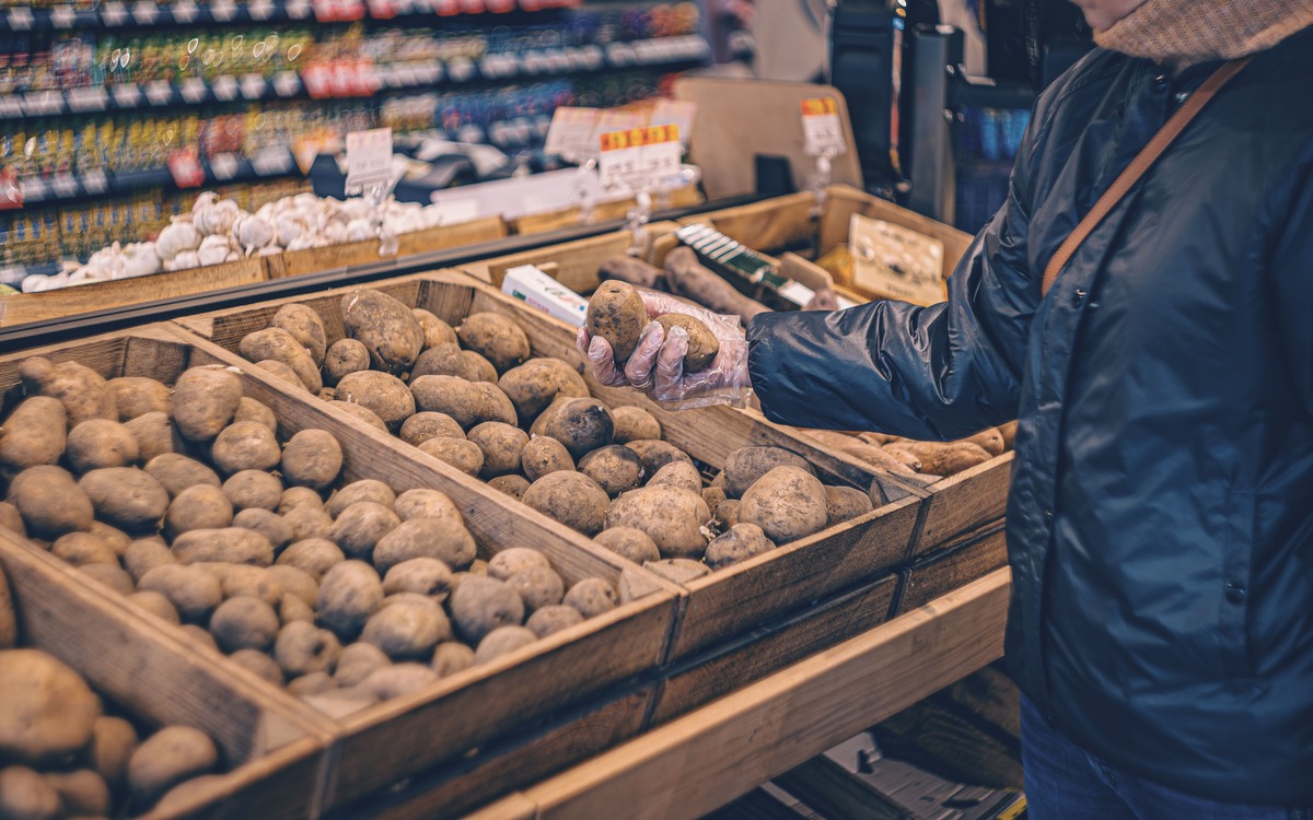Shopper selecting firm potatoes from wooden produce bins in a grocery store